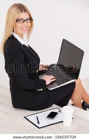 Busy and confident. Top view of confident mature businesswoman looking over shoulder and smiling while sitting at the staircase and working on laptop