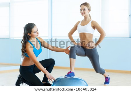 Exercising with fitness ball. Beautiful young woman in sports clothing exercising with personal trainer