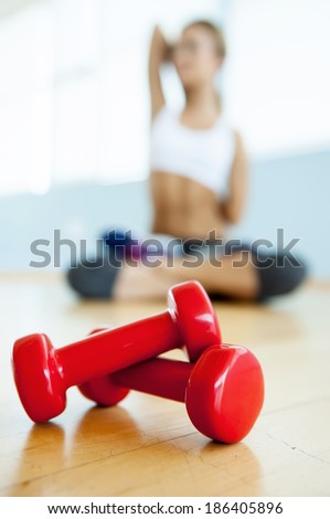 Sport and fitness concept. Close up image of dumbbell lying on the floor while young woman stretching on background