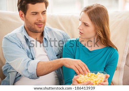 I am not sharing food! Beautiful young couple sitting on the couch together and watching TV