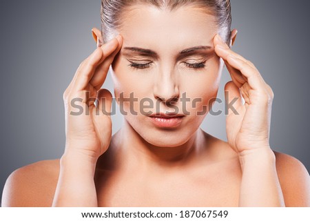 Awful headache. Mature shirtless woman holding head in hands and keeping eyes closed while standing against grey background