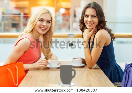 Relaxing after shopping. Two beautiful young women drinking coffee at the restaurant and looking at camera
