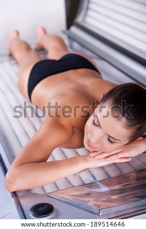 Beauty on tanning bed. Top view of beautiful young shirtless woman lying on tanning bed and keeping eyes closed