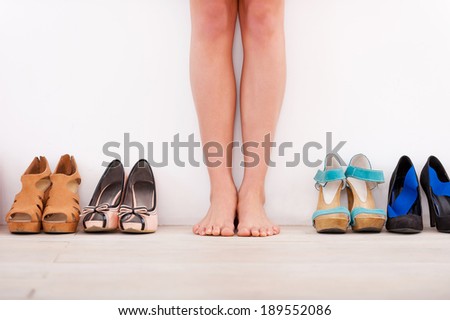 Making her choice. Cropped image of young woman standing against the wall while different shoes laying in a row near her