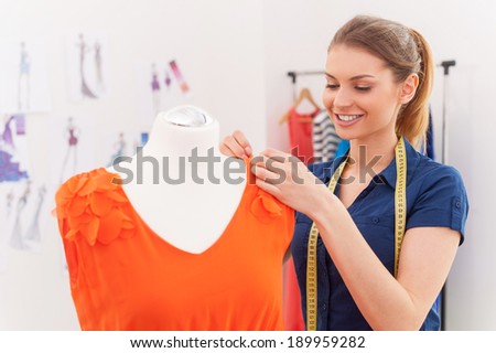 Designer at work. Beautiful female fashion designer adjusting dress on the mannequin and smiling
