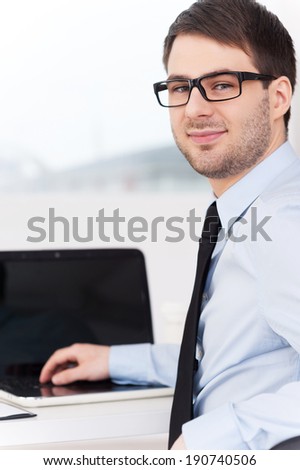 Confident businessman. Rear view of cheerful young man in shirt and tie looking over shoulder while sitting at his working place