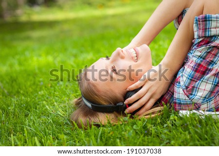 Enjoying music in nature. Side view of beautiful young woman in headphones listening to the music and smiling while lying on the green grass