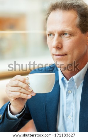 Relaxing with cup of fresh coffee. Thoughtful mature man in formalwear drinking coffee and looking away while sitting in coffee shop