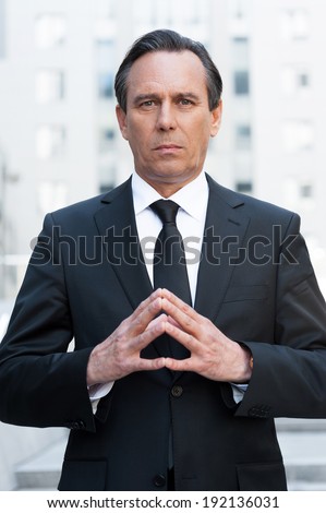 Power and success. Confident mature man in formal wear holding hands clasped and looking at camera while standing outdoors