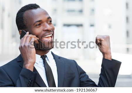 Great news! Happy young African man in formal wear talking on the mobile phone and expressing positivity while standing outdoors
