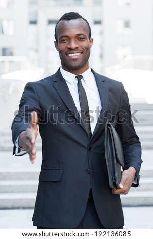 Welcome on board! Handsome young African man in full suit stretching out hand for shaking while standing outdoors