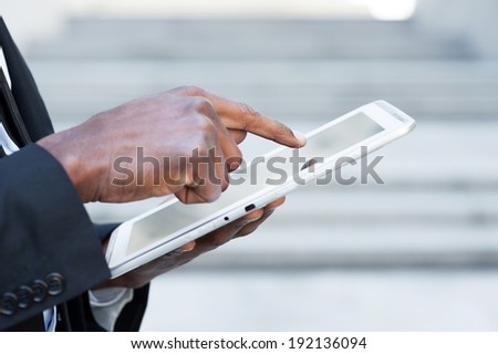 Working on tablet. Side view cropped image of African man in formal wear working on digital tablet while standing outdoors