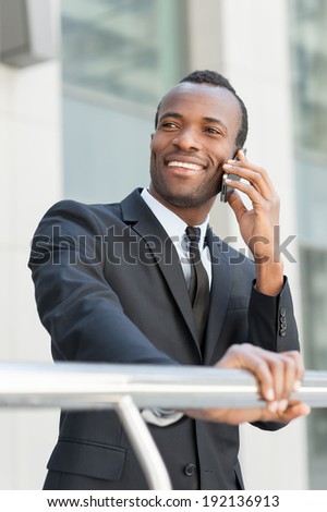 Happy about business going. Handsome young African man in formal wear talking on the mobile phone and smiling while standing outdoors