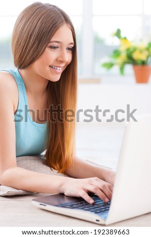 Surfing the net at home. Beautiful young teenage girl using computer while lying down on the floor at her apartment