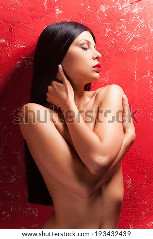 Naturally beautiful. Beautiful young shirtless woman covering breast with hands and keeping eyes closed while standing against red background