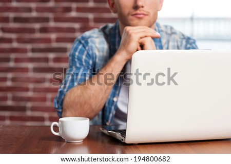 Finding out solution. Close-up of young man sitting at the table with laptop on it