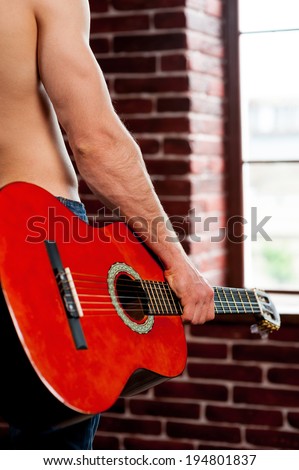 Guitar head. Close-up rear view image of shirtless man holding acoustic guitar while standing in front of the window