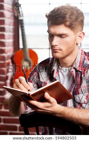 Creative composer. Handsome young man writing something in note pad while acoustic guitar laying in the background