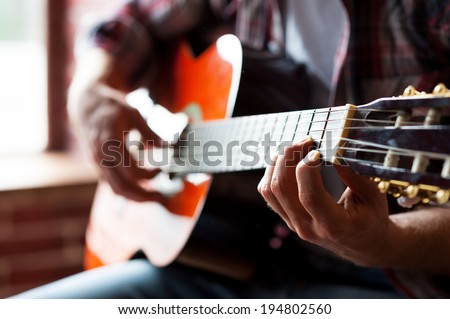Man playing guitar. Close-up of man playing acoustic guitar while sitting in front of the window