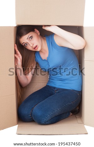 Trapped inside. Shocked young woman looking at camera while sitting in a cardboard box