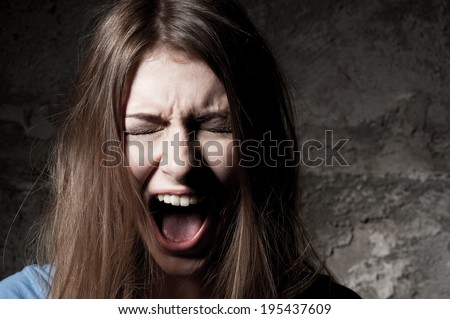 Terrified woman. Terrified young woman keeping eyes closed and shouting while standing against dark background