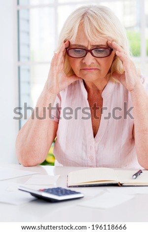 Financial troubles. Frustrated senior woman holding head in hands and looking at the bills laying on the table