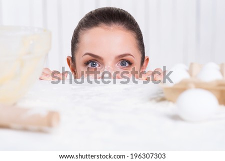Messy cooking. Playful young woman with flavor on face looking out of the kitchen table