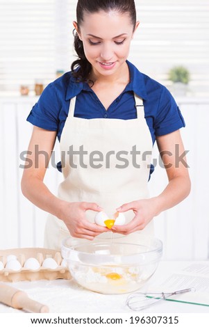 Making homemade pastry. Attractive young woman cracking egg into a bowl