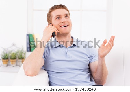 I am so glad to hear you! Cheerful young man talking on the mobile phone and gesturing while sitting on the couch