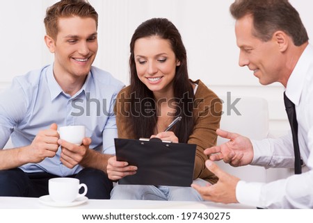 Signing a contract. Happy young couple signing documents while confident mature man in shirt and tie gesturing and smiling