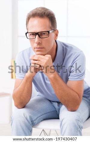 Confident expert. Confident casual businessman in glasses holding his hands on chin and looking at camera while sitting on the chair