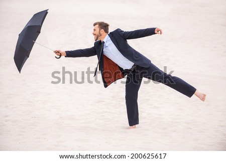 Gentleman with umbrella. Playful young man in formalwear holding umbrella while standing in desert