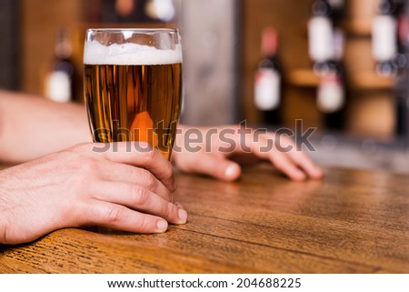 Quenching his thirst. Close-up of man holding glass with beer while standing at the bar counter