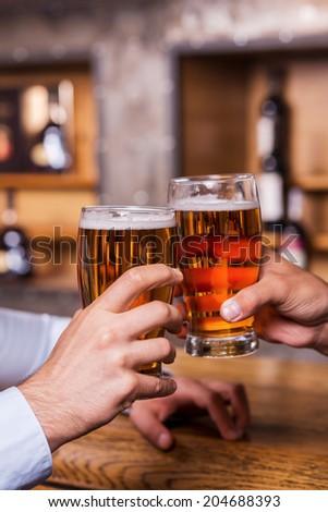 Cheers! Close-up of two men toasting with beer at the bar counter