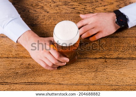Beer time. Top view of male hands holding beer glass on the bar counter