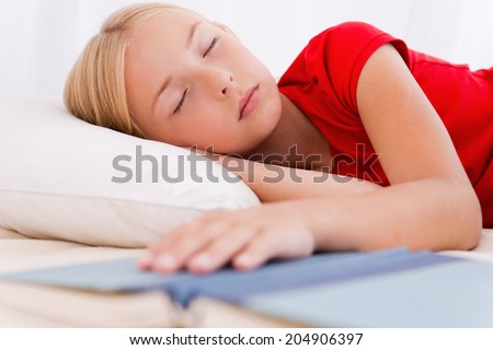 Little bookworm. Cute little girl sleeping while lying in bed and holding hand on book