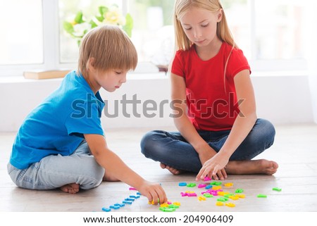 Playing and studying. Two cute little children playing with plastic colorful letters while sitting on the hardwood floor