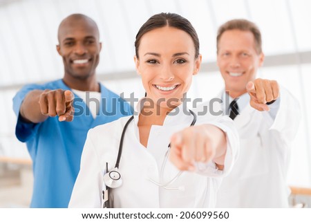 Ready to help you! Three cheerful doctors pointing you and smiling