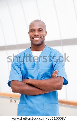 You can absolutely trust me. Confident young African doctor in blue uniform looking at camera and keeping arms crossed