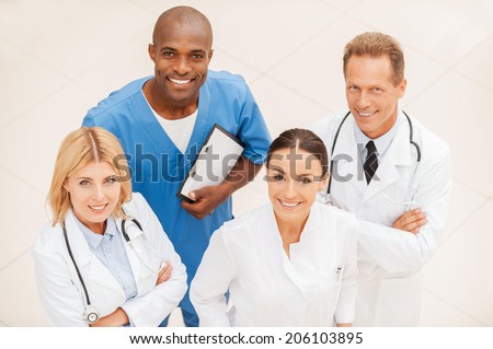 Ready to help you anytime. Top view of four confident doctors standing close to each other and smiling