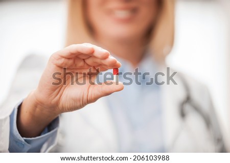 Take this pill! Close-up of female doctor in white uniform holding pill and smiling while