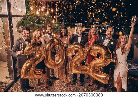 Group of beautiful people in formalwear carrying gold colored numbers and smiling