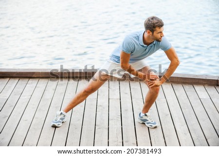 Stretching exercises. Confident young man doing stretching exercises while standing on quayside