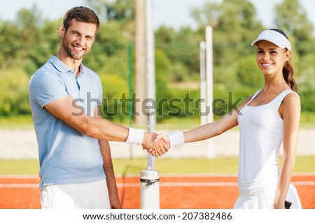 Friendship wins. Two confident tennis players shaking hands and smiling while standing near the tennis net
