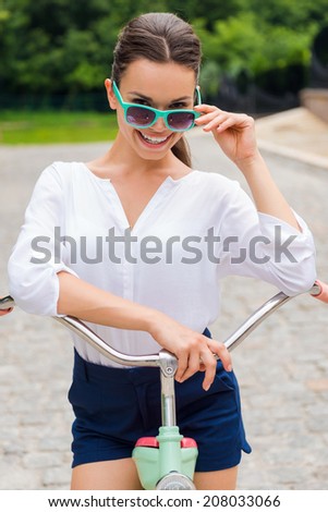 In her own style. Attractive young smiling woman adjusting her sunglasses while leaning at her vintage bicycle in park