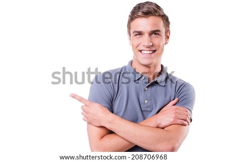 Look at this! Handsome young man pointing away and smiling while standing isolated on white background