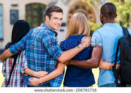 We are good friends. Rear view of handsome young man looking over shoulder and smiling while walking together with friends