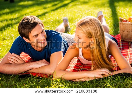 Enjoying their perfect date together. Happy young loving couple relaxing in park together while lying on picnic blanket and looking at each other