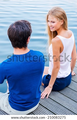 Having a romantic date. Top view of beautiful young loving couple sitting at the quayside together and looking at each other with smile