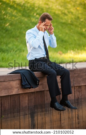 Depressed businessman. Depressed mature businessman holding head in hands while sitting at the quayside